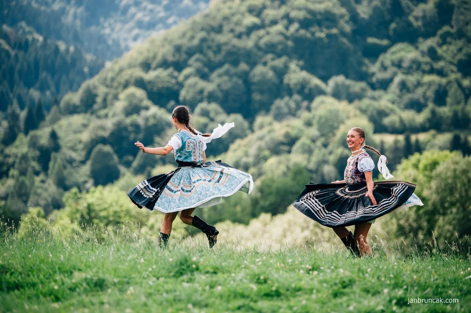 Two dancers in Slovak folk costumes spinning on a green hillside